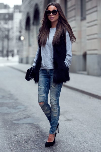 black faux fur vest with gray sweatshirt and torn slim fit jeans