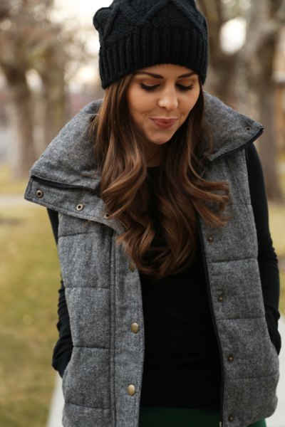 black knitted hat with a gray quilted long vest and knitted sweater