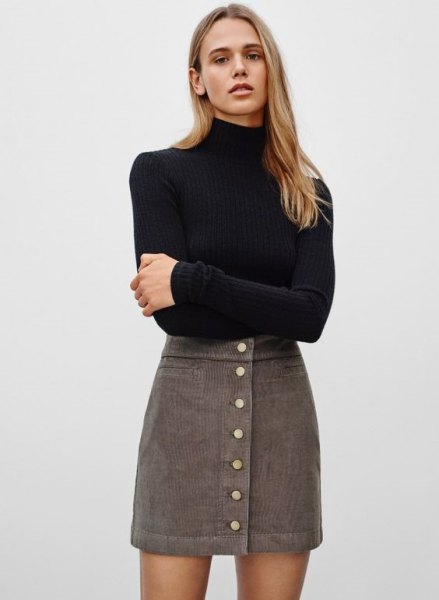 black, figure-hugging sweater with stand-up collar and gray, high-waisted mini-cord skirt