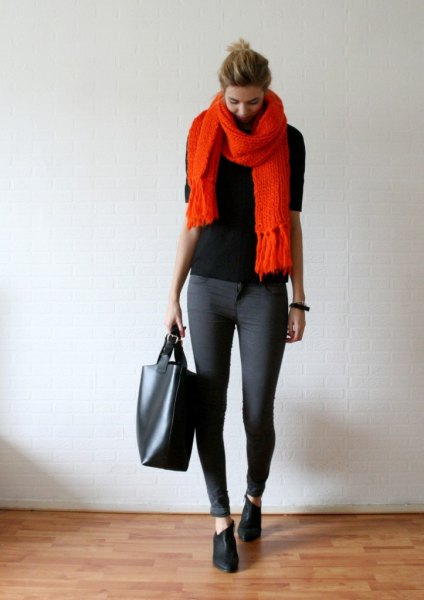 black sweater with an orange fringed scarf and gray skinny jeans