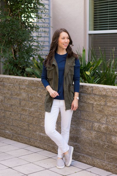 brown utility vest with dark blue long-sleeved top and white jeans