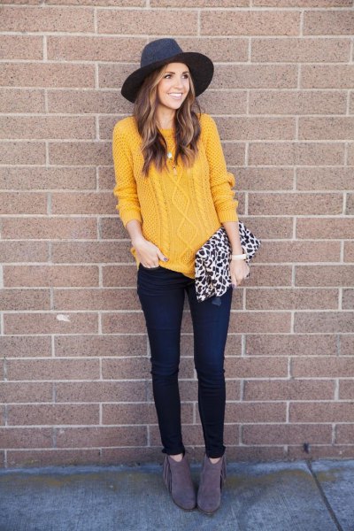 Cable knit sweater with a black felt hat and thin dark jeans