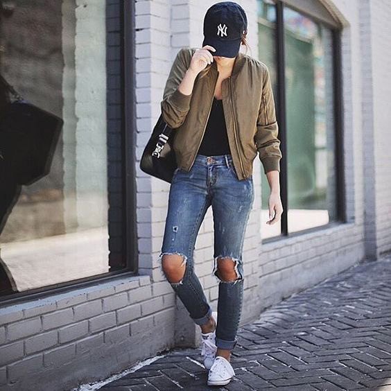 Green bomber jacket with a black top with a scoop neckline and heavily ripped jeans