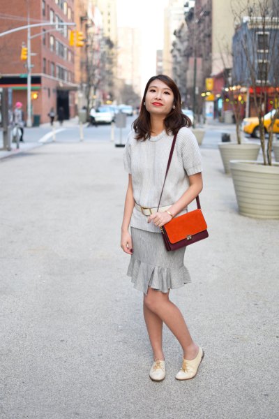 Ivory short-sleeved sweater with a gray frilled mini skirt and white oxford leather shoes
