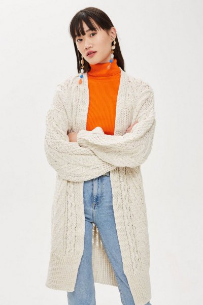 Cream-colored long knitted cardigan with an orange sweater and mom jeans