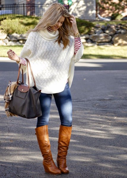 white cable knit poncho sweater with blue skinny jeans and knee-high boots made of brown leather
