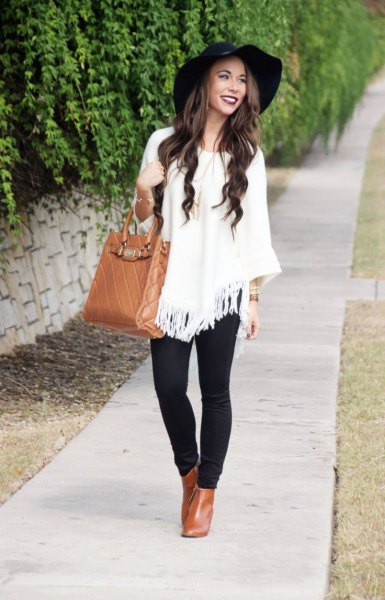 white poncho sweater with fringes and black floppy hat